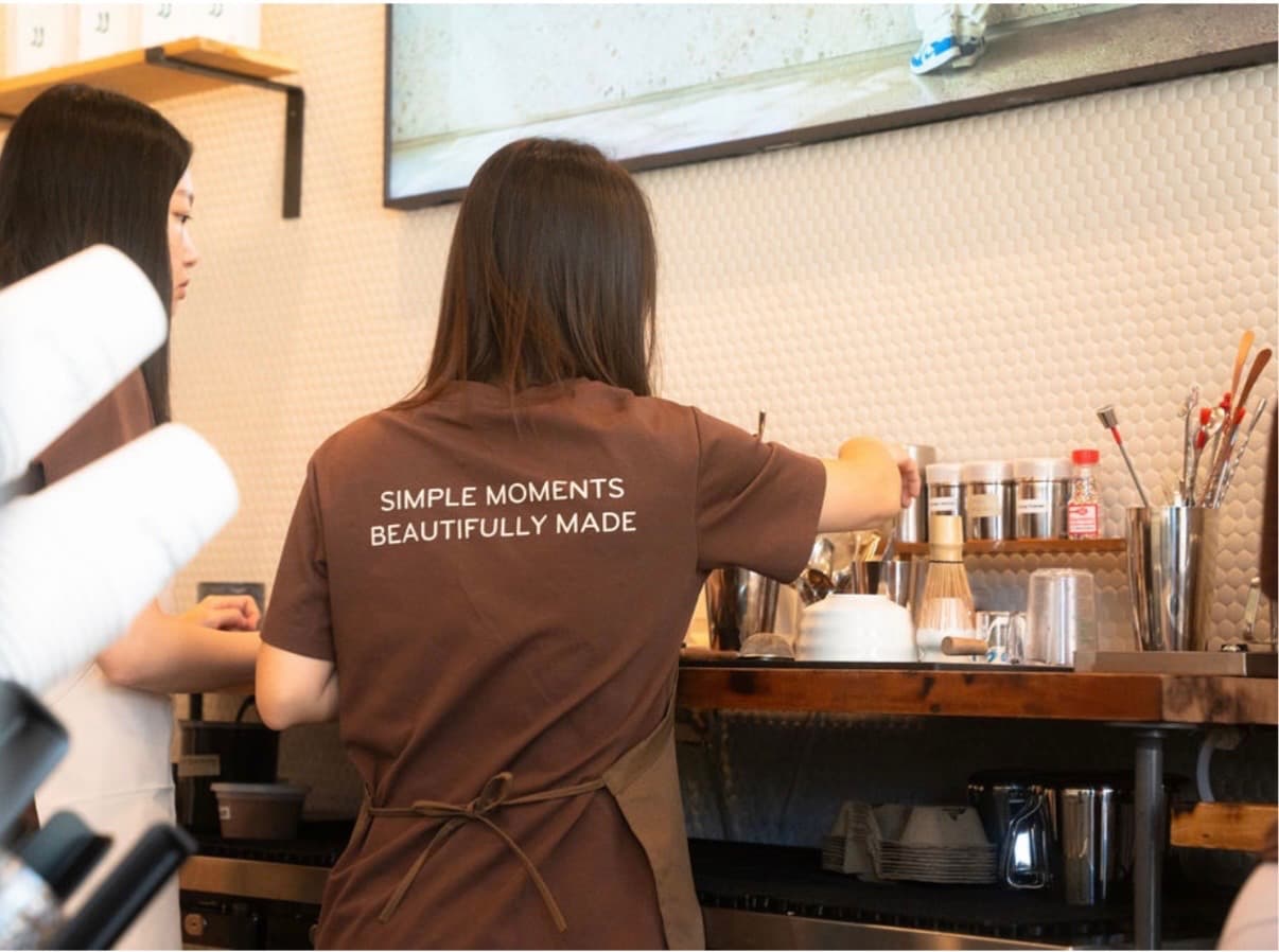 A barista in a Simple Moments, Beautifully Made shirt working the matcha bar