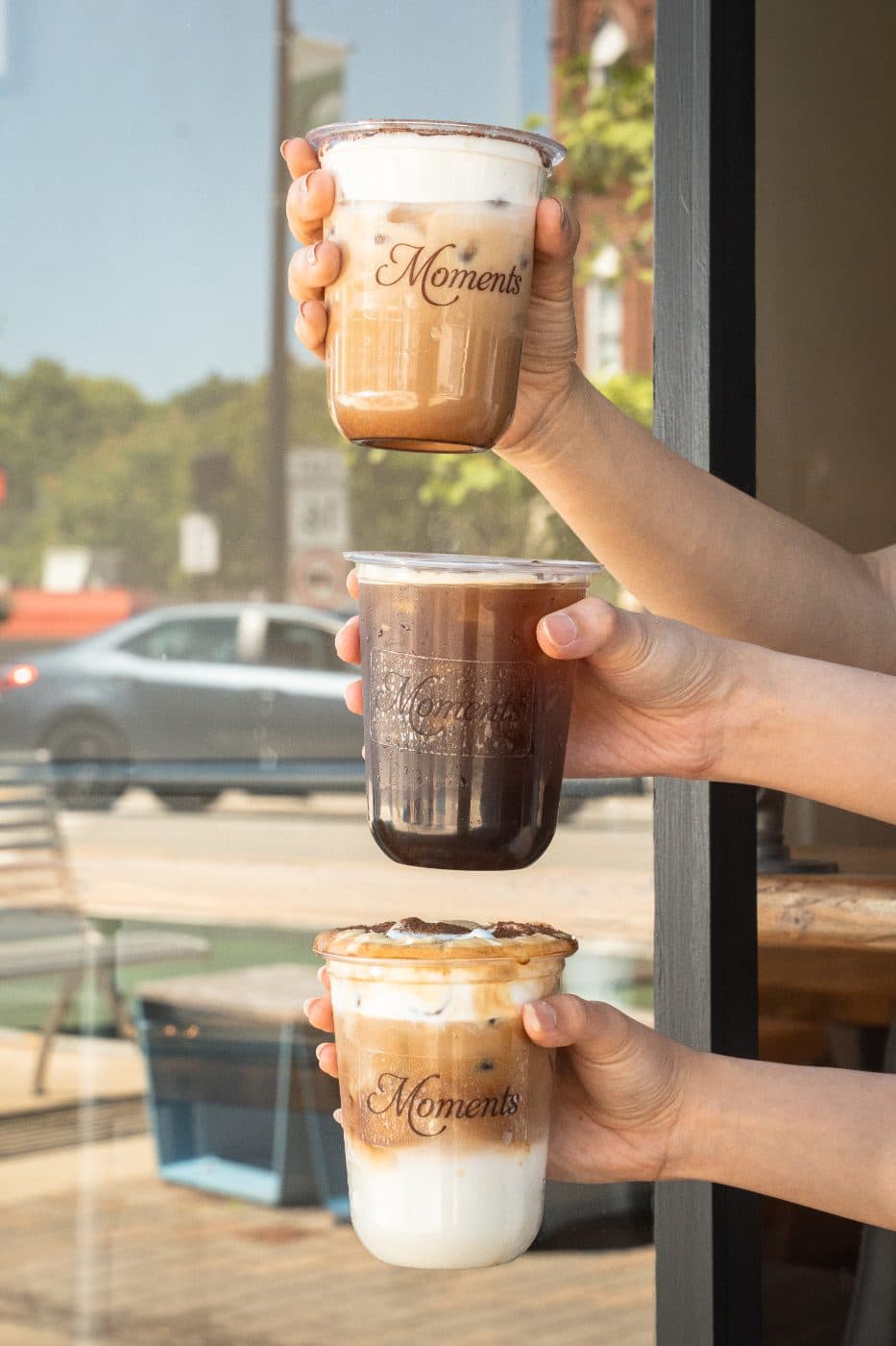 Three iced Moments drinks held up in a stack outside the cafe window